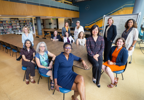 A group picture of 14 women holding leadership positions in the College of Engineering gathered around a table in the library.