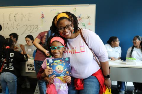 Young author Soleil A. Cross holds her book, Pluto, Special, Just the Same Dwarf Planet, as she explores the Brain Games exhibit with her mom.