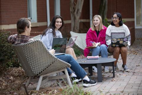 Group of students sitting together outside with laptops smiling.