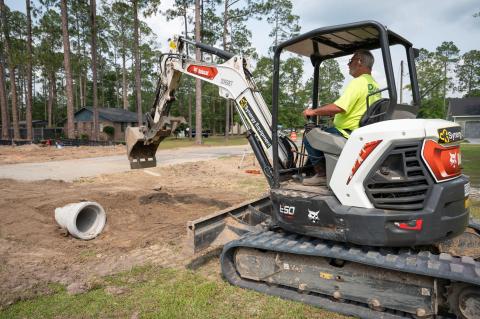 This image shows a worker in a small excavator preparing the area around a drainage pipe