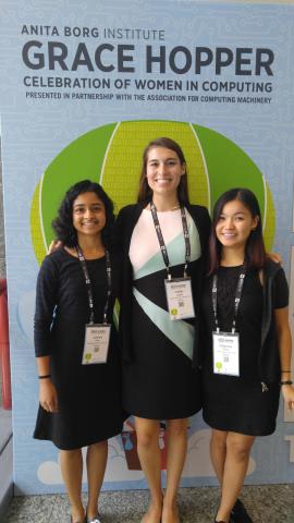 Lakshmi Raju, Caitlyn Caggia, and Delgermaa Nergui pose in front of a conference sign.