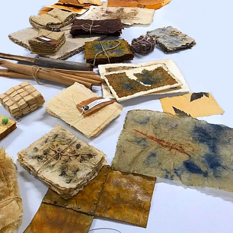 Handmade papers with patterns and designs made from natural dyes are scattered across the image.