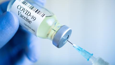 A vial labeled "Covid-19 vaccine" with a syringe inserted.