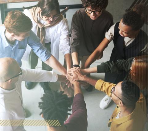 Diverse team of individuals in a circle with their hands stacked together in the middle of the circle