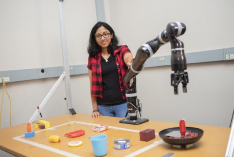 Georgia Tech Ph.D student Lakshmi Nair behind robotic arm picking up objects from tabletop