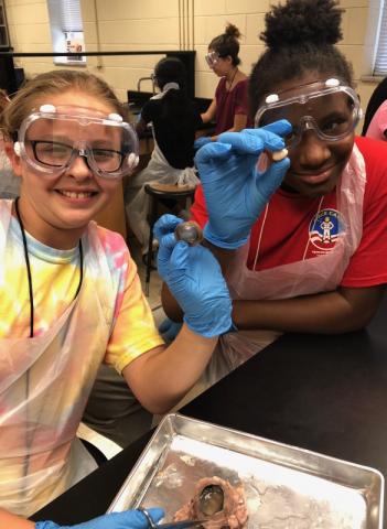 Two young female students wearing googles and gloves in a science lab