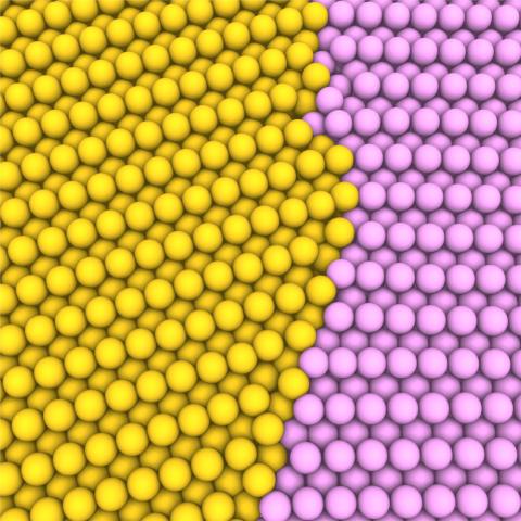 A graphic with yellow and pink spheres in a crystal formation, representing a grain boundary between two abutting grains