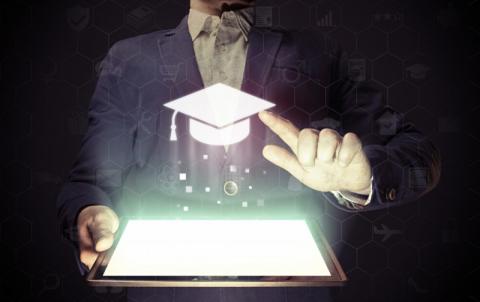 Glowing tablet with person touching 3D projected image of commencement cap.