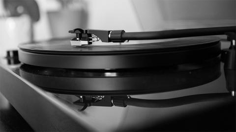 A black and white photograph of a vinyl record on a turntable. It is in closeup, the turntable and record reflected as a duplicate on the shiny surface.