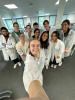 A group of people gathering for a smiling selfie while wearing lab coats and gloves.