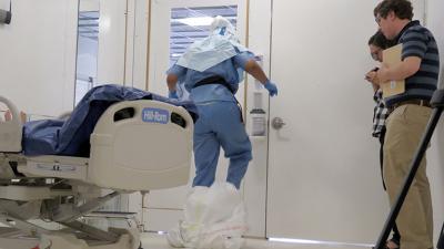A researcher observes a doffing simulation in a mock-up of a biocontainment unit.