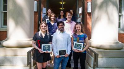 Student award winners stand on the staircase in front of the Swann Building holding their plaques.