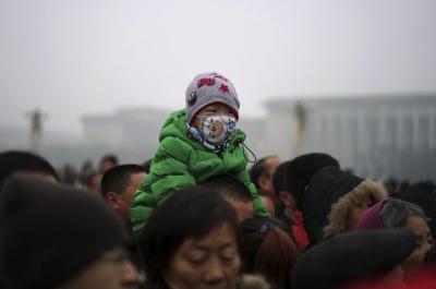 A boy wearing a mask sits on the shoulders of a man as they watch a flag-raising ceremony amid heavy smog at the Tiananmen Square, after the city issued its first ever “red alert” for air pollution, in Beijing, China. Photo by Reuters