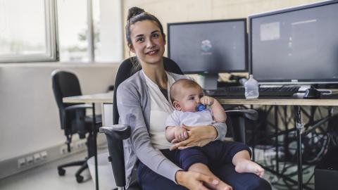 A woman with a baby on her lap poses for a photo in an office.