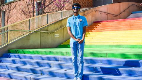 A student wearing a blue shirt and rainbow button stands on the rainbow steps outside Klaus Advanced Computing Building