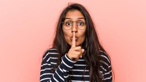 A young woman makes a shushing gesture