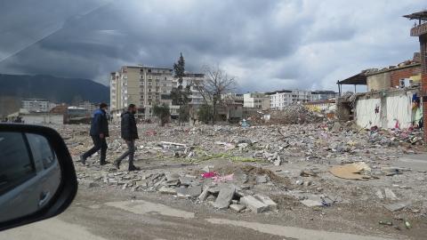 Photo of two men walking through a field of fallen buildings with most taken down to rubble.