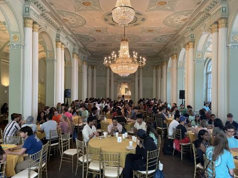 A picture of Honors Program students at the 2022 first-year student retreat. The students are sitting at round tables in a large ballroom space, located in the Biltmore Ballrooms