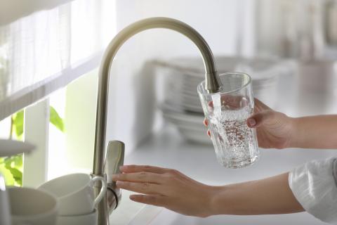 A person filling a glass of water from a faucet 