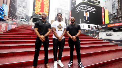 Antwan Owens posing with two men from the company that endorsed him in front of a sign in Times Square about the deal.