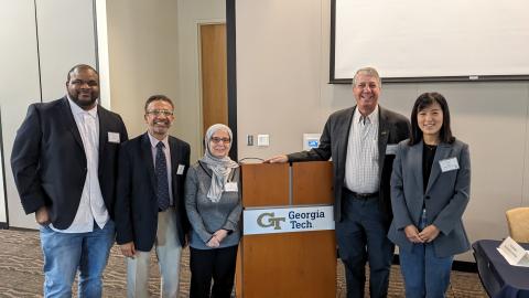 Five people stand in a room next to a podium.