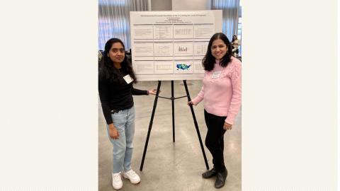 A graduate student and her professor flank a research poster on a tripod.