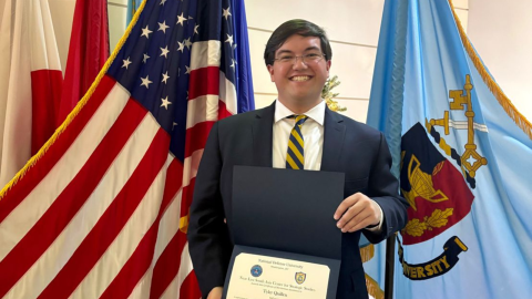Tyler holding a certificate in front of flags in a state capitol / government building setting