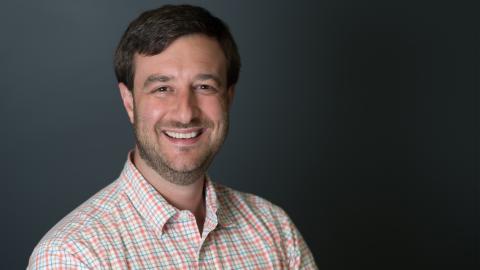 A man in a checked shirt smiles at the camera.