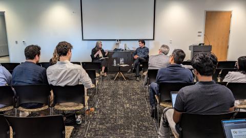 Two people talking in front of a seated audience