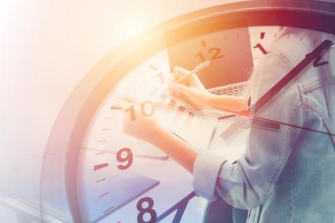 Clock with person writing in notebook in background.