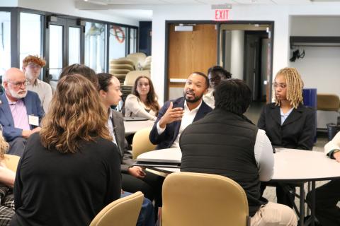 A man gestures with his hands as he speaks to a table of students and alumni.