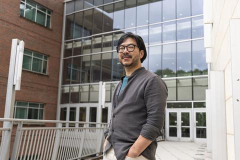 Eric Shen, a Georgia Tech researcher, standing in front of the MoSE Building, an academic building with numerous glass windows