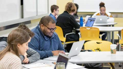 Students seated at tables look at their laptops during a class.