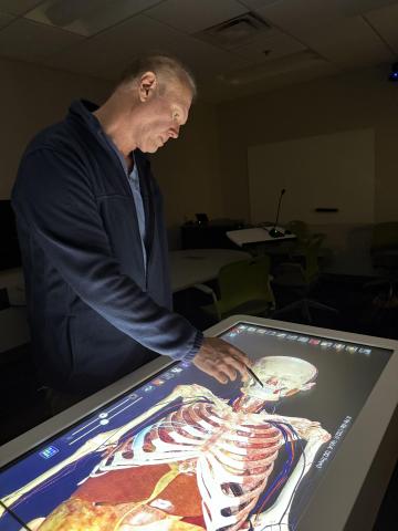 Man standing over table embedded with 3-D skeleton.