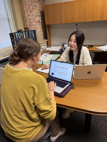 Two women sit opposite each other at a desk with a computer in the middle.