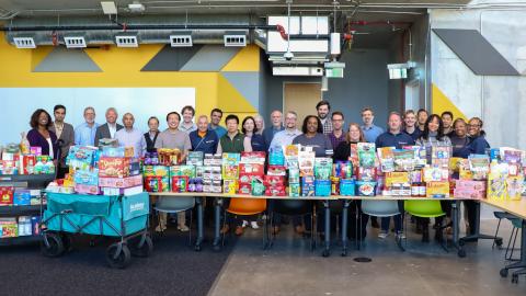1.	A photo of a group of people standing behind a table full of packaged food. The group is smiling and represents a diverse crowd of faculty and staff.
