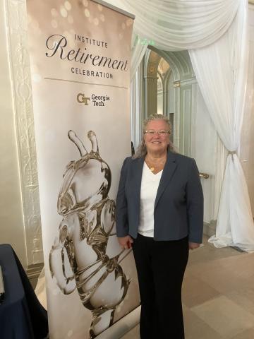 Jill Gostin posing beside the banner at the Georgia Tech Retirement Celebration.