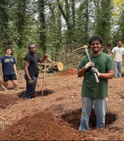 Four students holding pickaxes stand in holes.