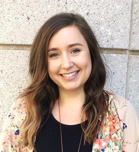 A smiling woman with long brown hair, wearing a black t-shirt and a floral cardigan