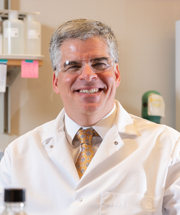 A man with a white lab coat and glasses on and a yellow-gold tie