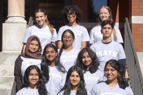 Eleven students sitting in rows in front of a brick building.
