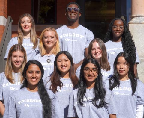 10 students standing in rows in front of brick building.