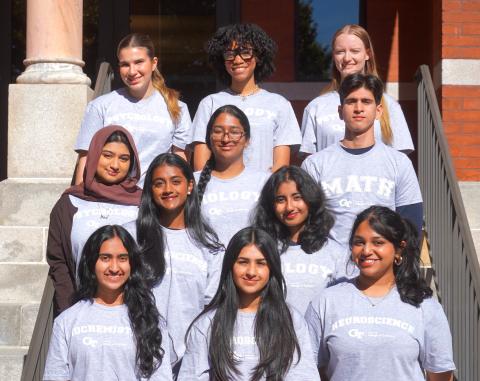 11 students standing in rows in front of brick building.