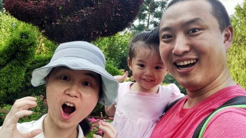 A young family poses for a photo in front of green vegetation