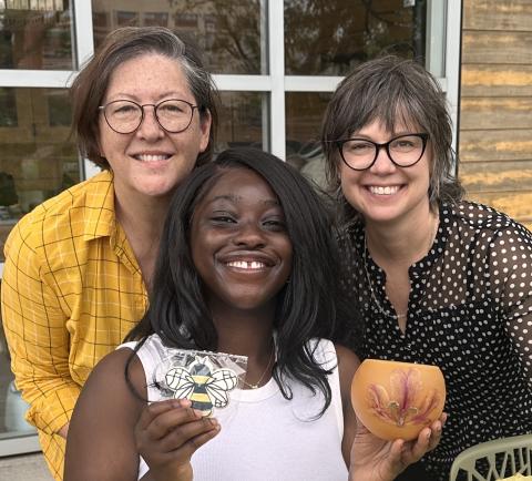 Three women with one of them holding beekeeping equipment.
