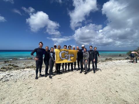 group of scuba trip attendees holding georgia tech flag on beach