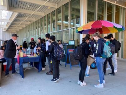 a group gathers by a rainbow umbrella for a tasting of sustainably sourced foods