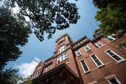 Tech Tower at the Georgia Institute of Technology, a red-brick academic building with white trim and arched windows, rising above surrounding trees under a blue sky.