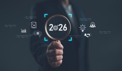 Businessman holding magnifying glass focusing on year 2026 with digital icons of innovation, AI, analytics, and global strategy. Concept of future planning, technology trends and vision. 