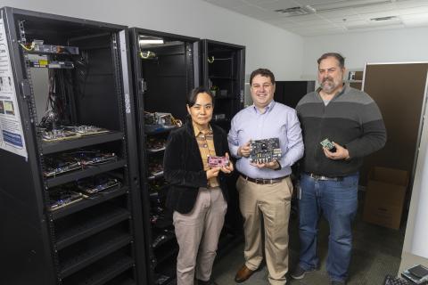Three researchers stand in front of a rack of computing equipment.